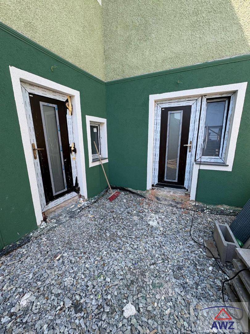 Ecke des Hauses mit grüner Fassade und zwei Türen, die zu einem Schotterbereich führen.