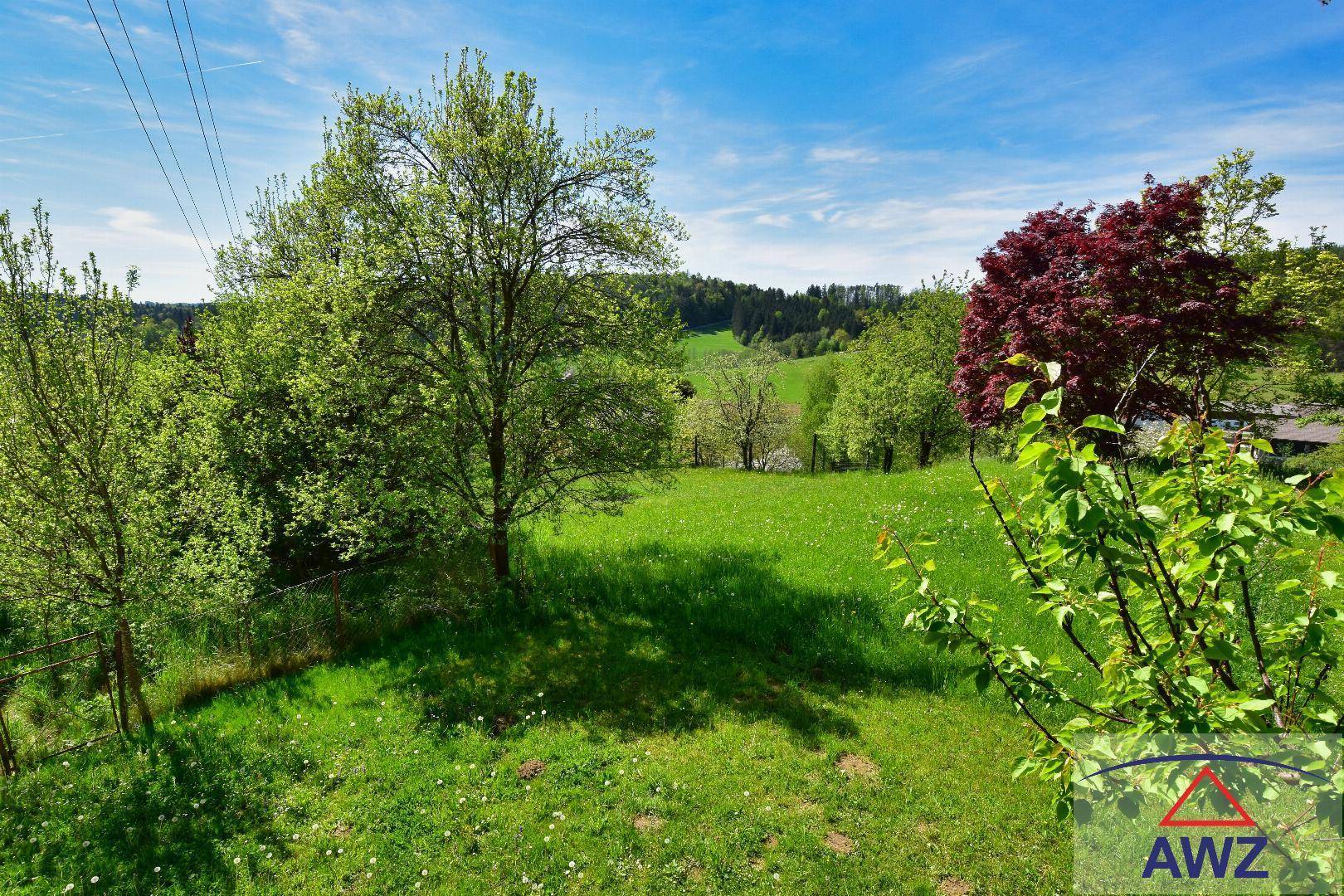 Weitläufiger Blick über grüne Wiesen und bewaldete Hügel unter blauem Himmel.