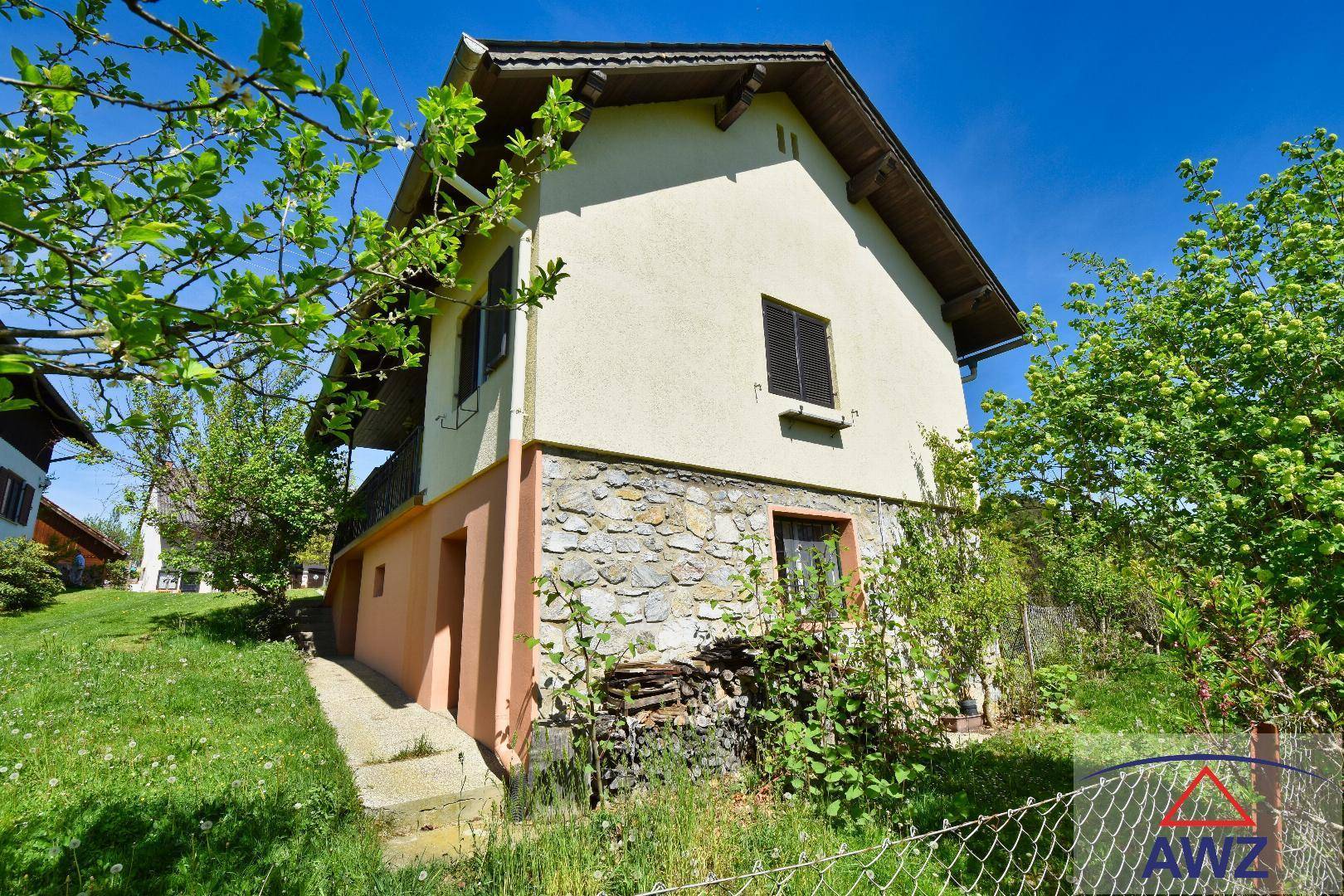 Seitenansicht des Hauses mit Steinfassade im unteren Bereich und grüner Umgebung.