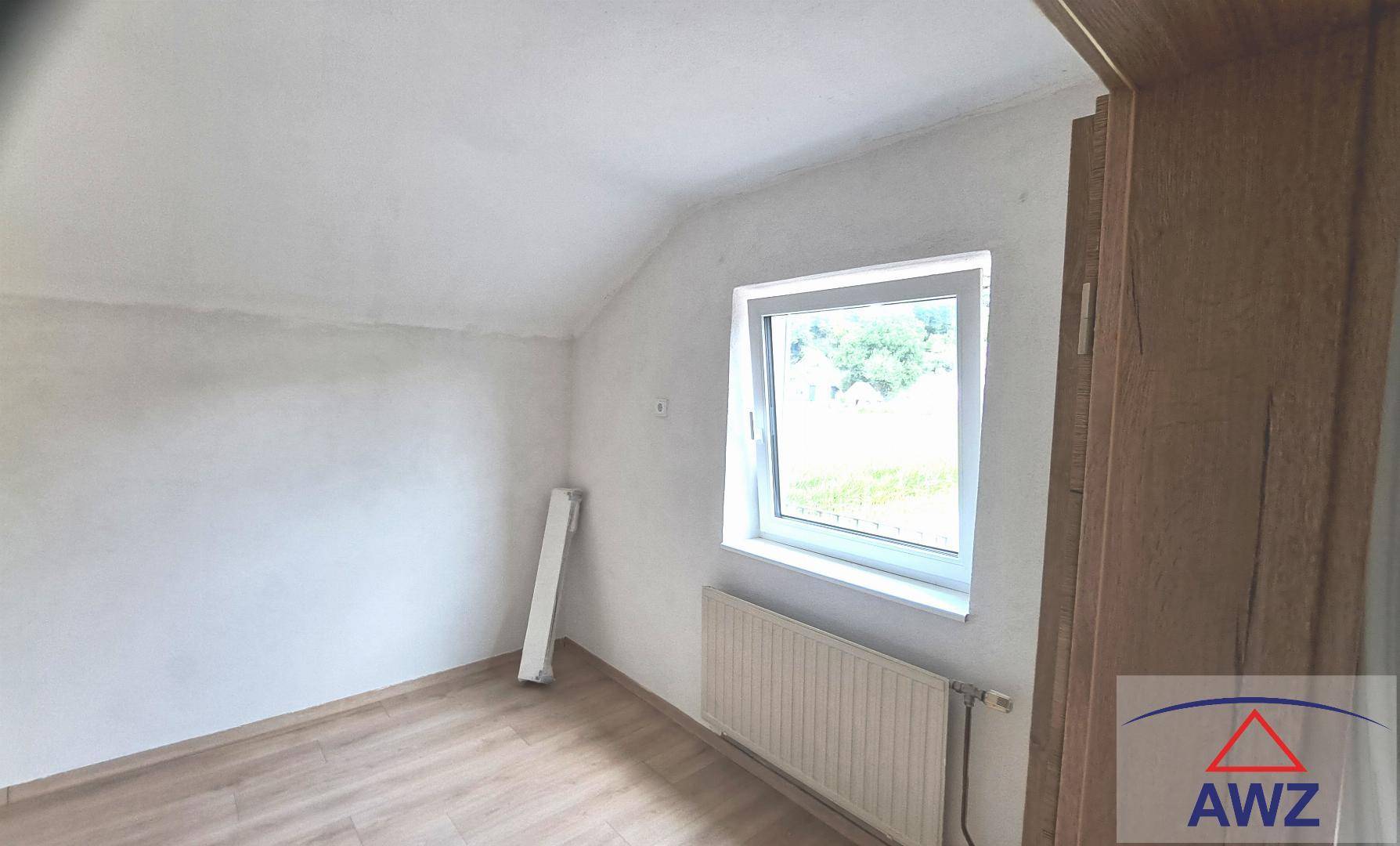 Dachgeschosszimmer mit schräger Decke, Laminatboden und einem Fenster für natürliches Licht.