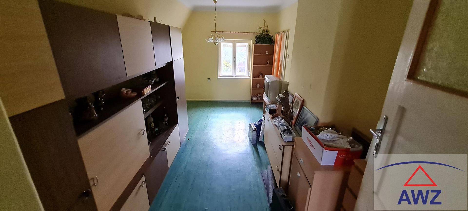 Langes Zimmer mit Schrankwand, Fenster und grünem Bodenbelag, hell beleuchtet.