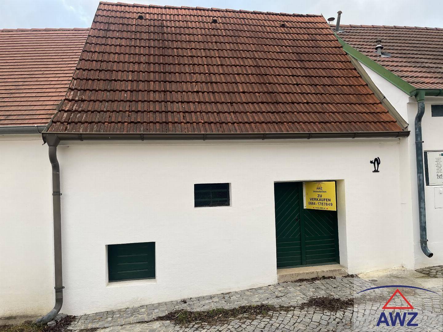 Weiß verputztes Gebäude mit rotem Ziegeldach und grünen Türen, zum Verkauf angeboten.