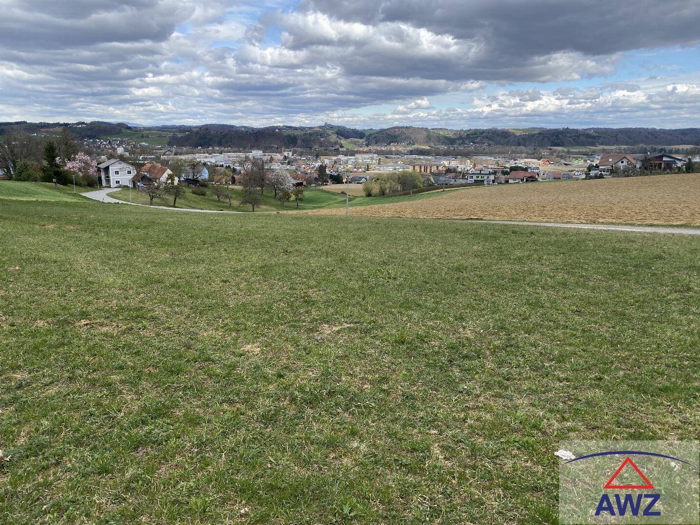 Offenes grünes Feld mit Panoramablick auf die ländliche Umgebung und eine entfernte Ortschaft.