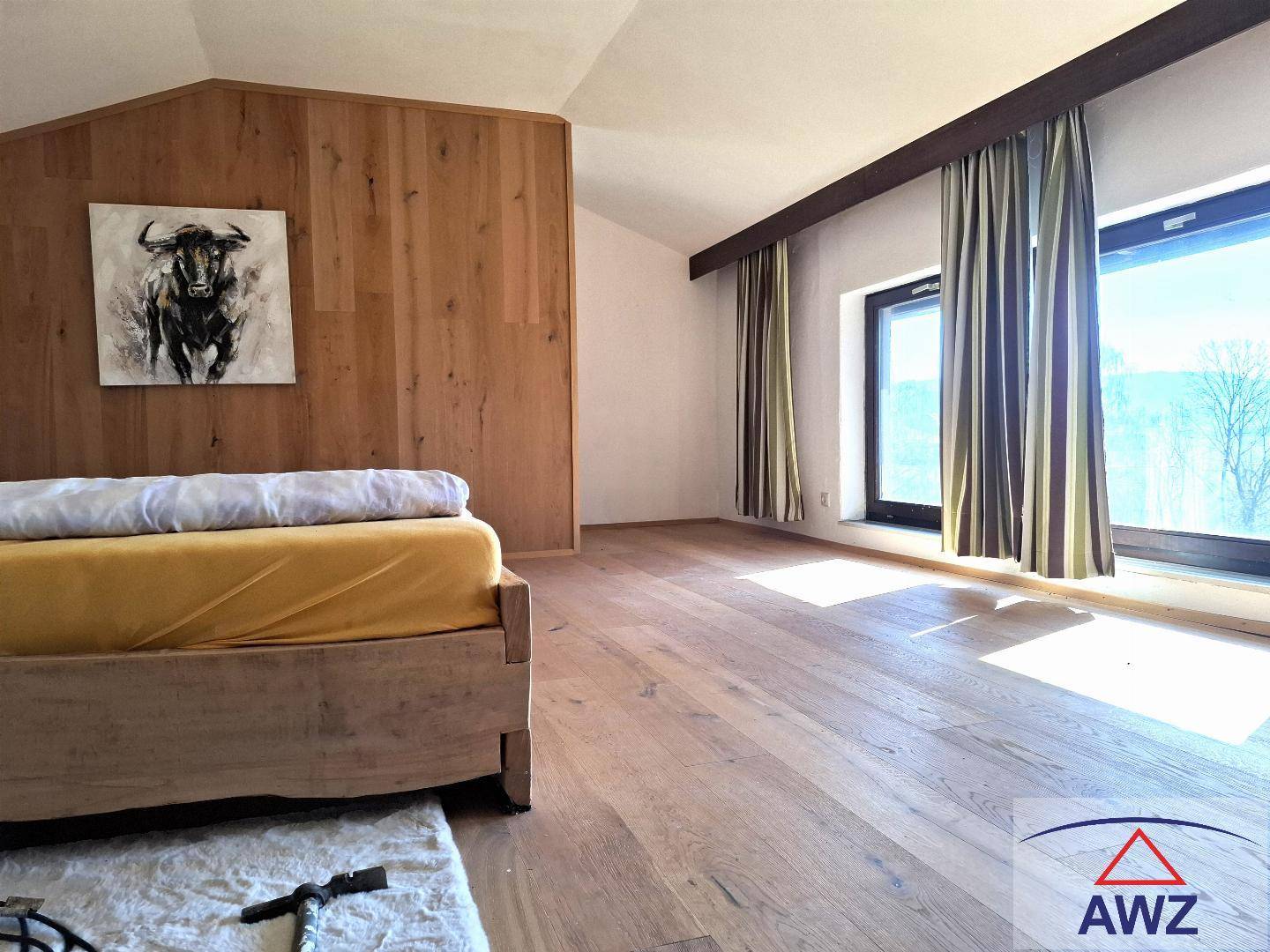 Helles Schlafzimmer mit Holzboden, Holzvertäfelung und schrägen Decken unter großen Fenstern.