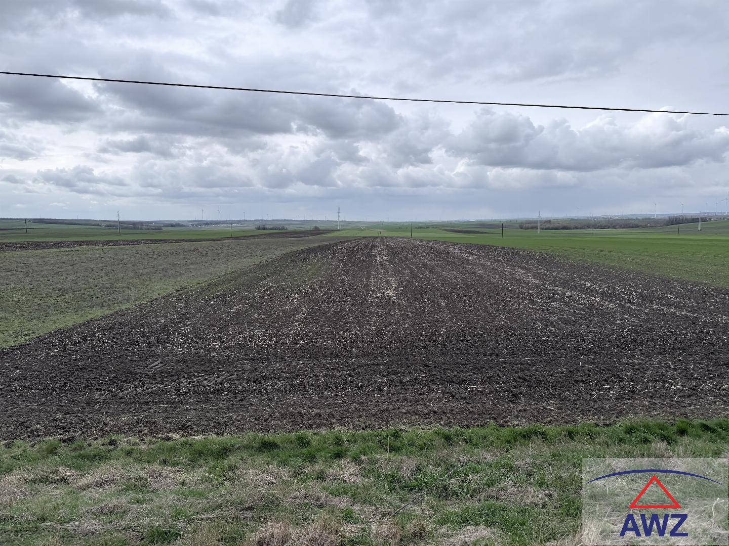 Weite Ackerlandschaft mit braunen und grünen Feldern unter einem dramatischen, bewölkten Himmel.