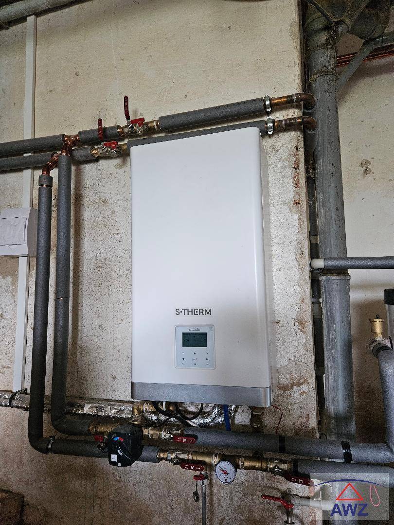 Warmwasserbereiter an einer Wand mit sichtbaren Rohrleitungen in einem Technikraum.