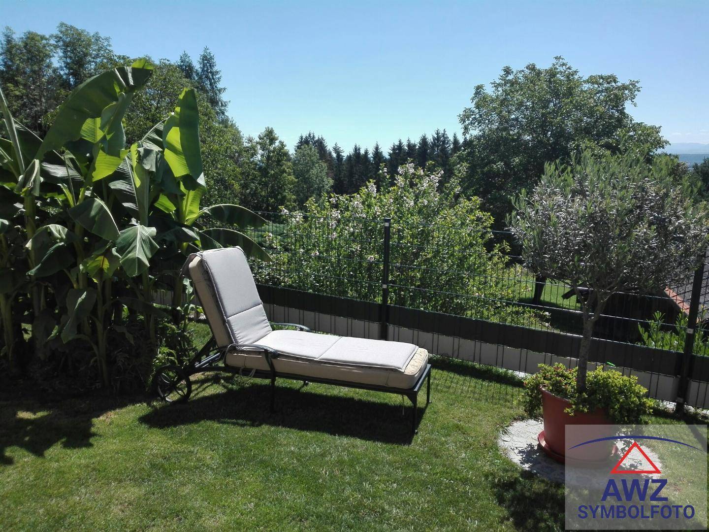 Sonniger Gartenbereich mit Liegestuhl und üppiger grüner Vegetation im Hintergrund.