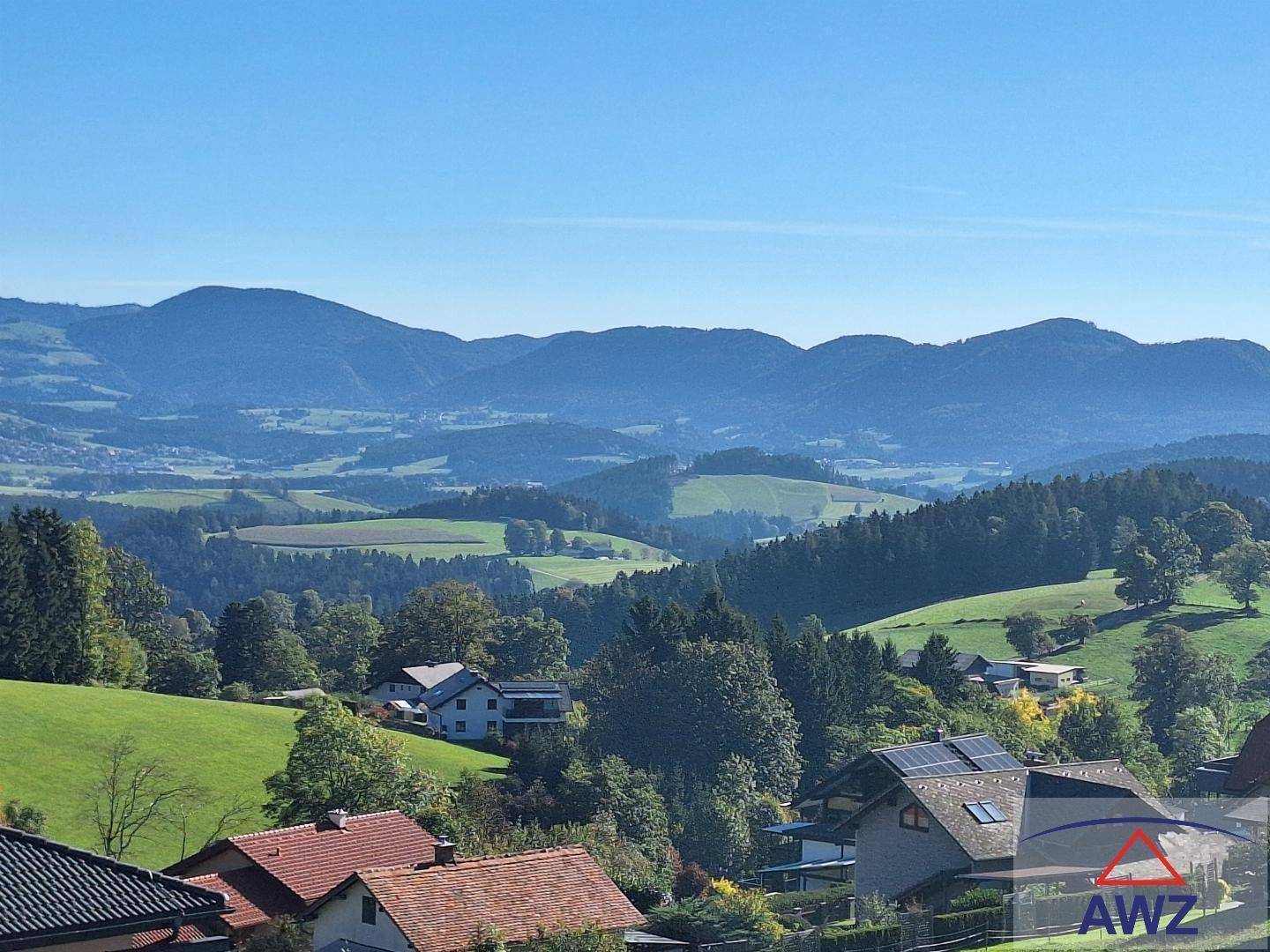 Malerischer Ausblick auf das Tal mit Häusern, grünen Hügeln und Bergen im Hintergrund.