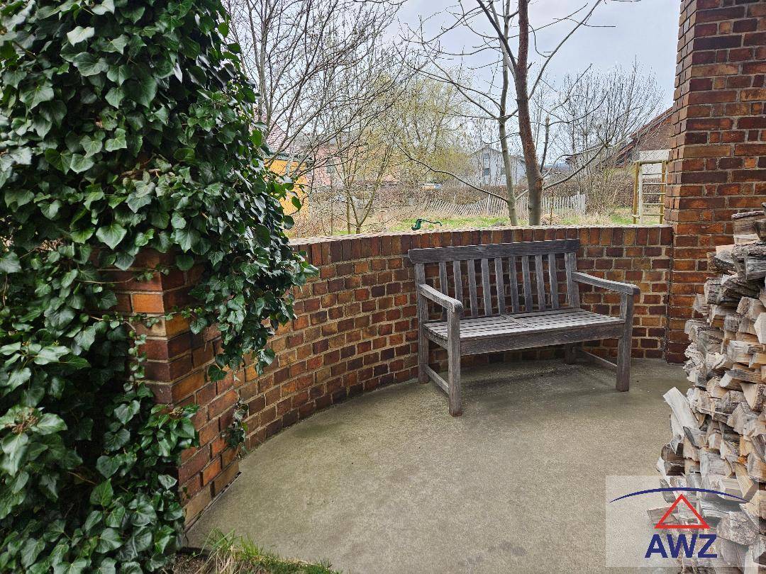 Gemütliche kleine Terrasse mit Holzsitzbank und gestapeltem Brennholz an einer Ziegelwand.