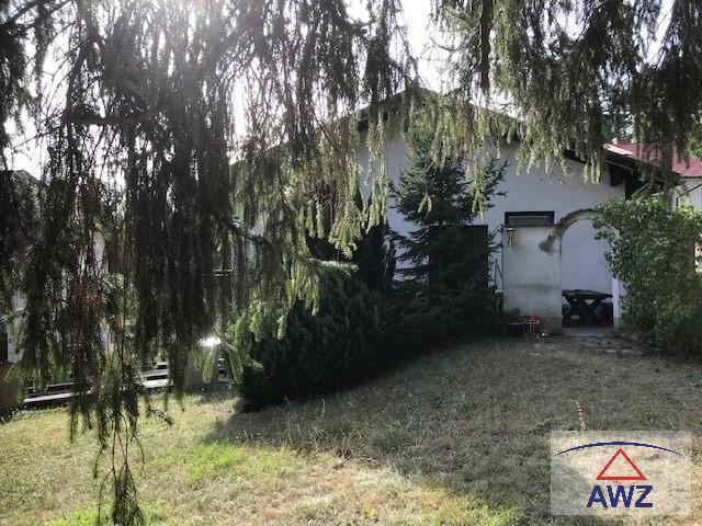 Hausfassade umgeben von Bäumen und einem Gartenbereich mit überdachtem Sitzplatz.