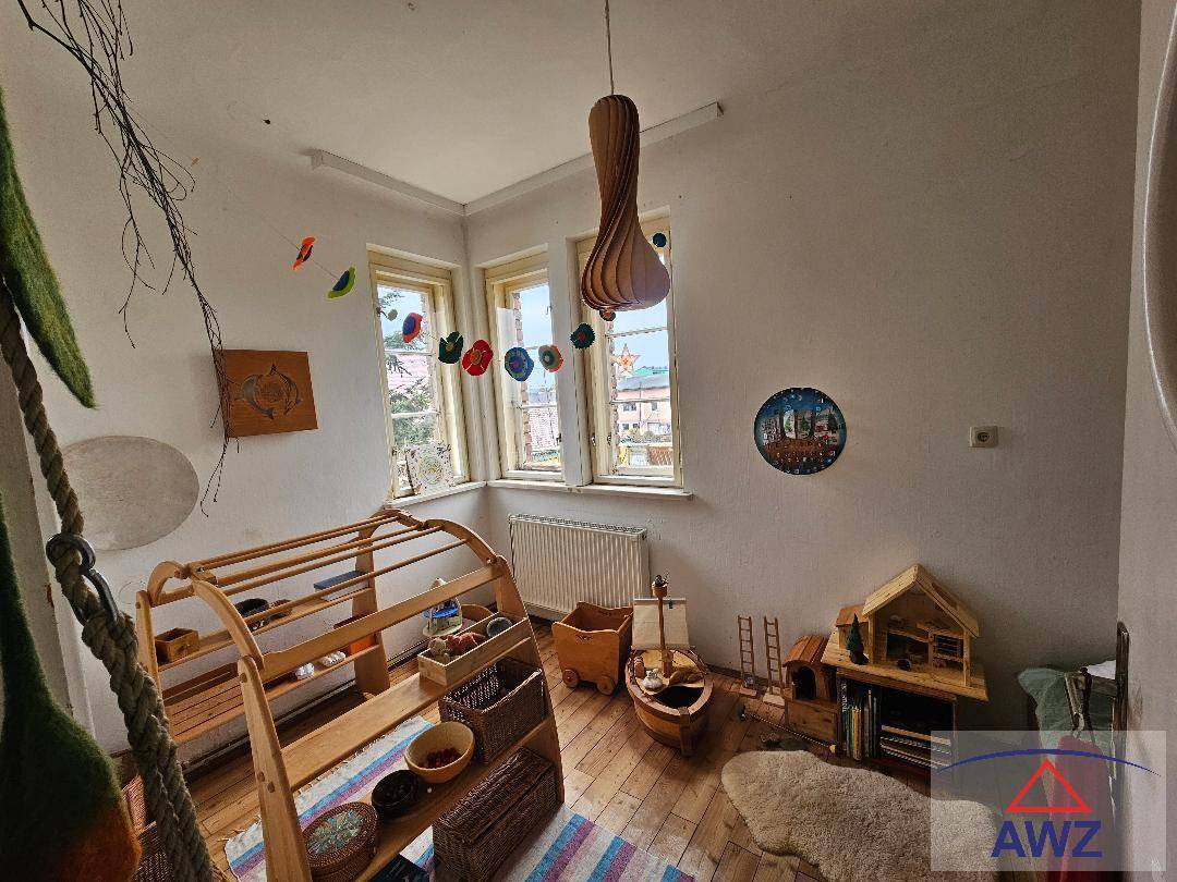 Helles Kinderzimmer mit Spielzeug, Holzregalen und großen Fenstern, die viel Licht hereinlassen.