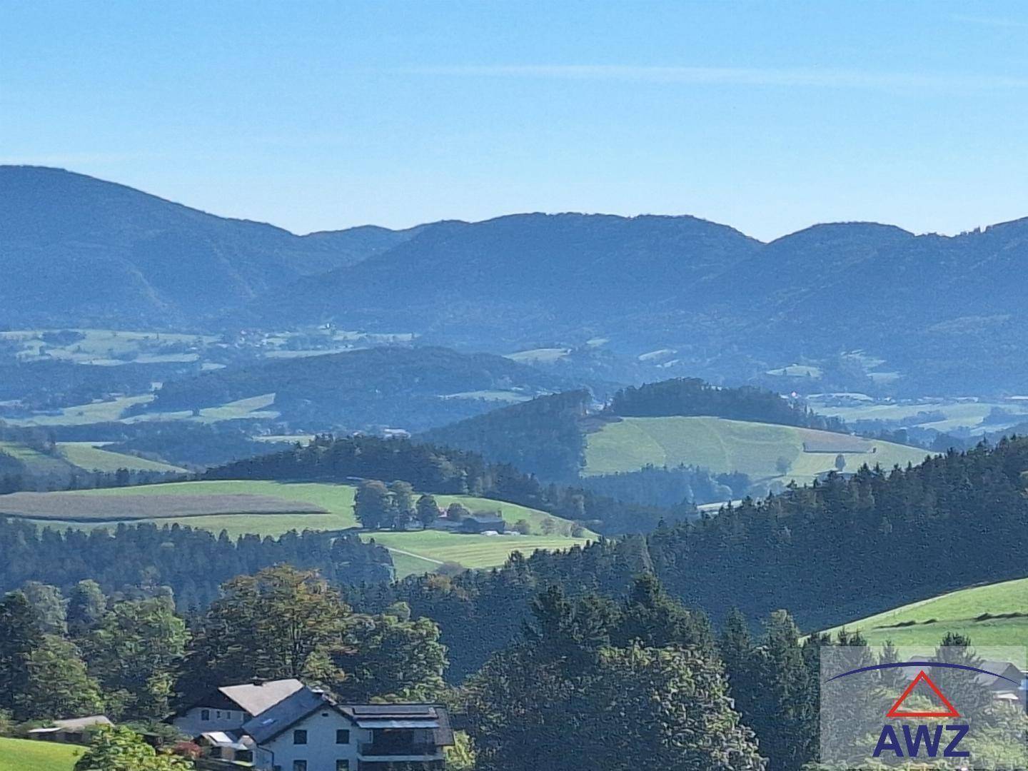 Weitläufiger Panoramablick über die hügelige Landschaft mit Bergen und vereinzelten Häusern.