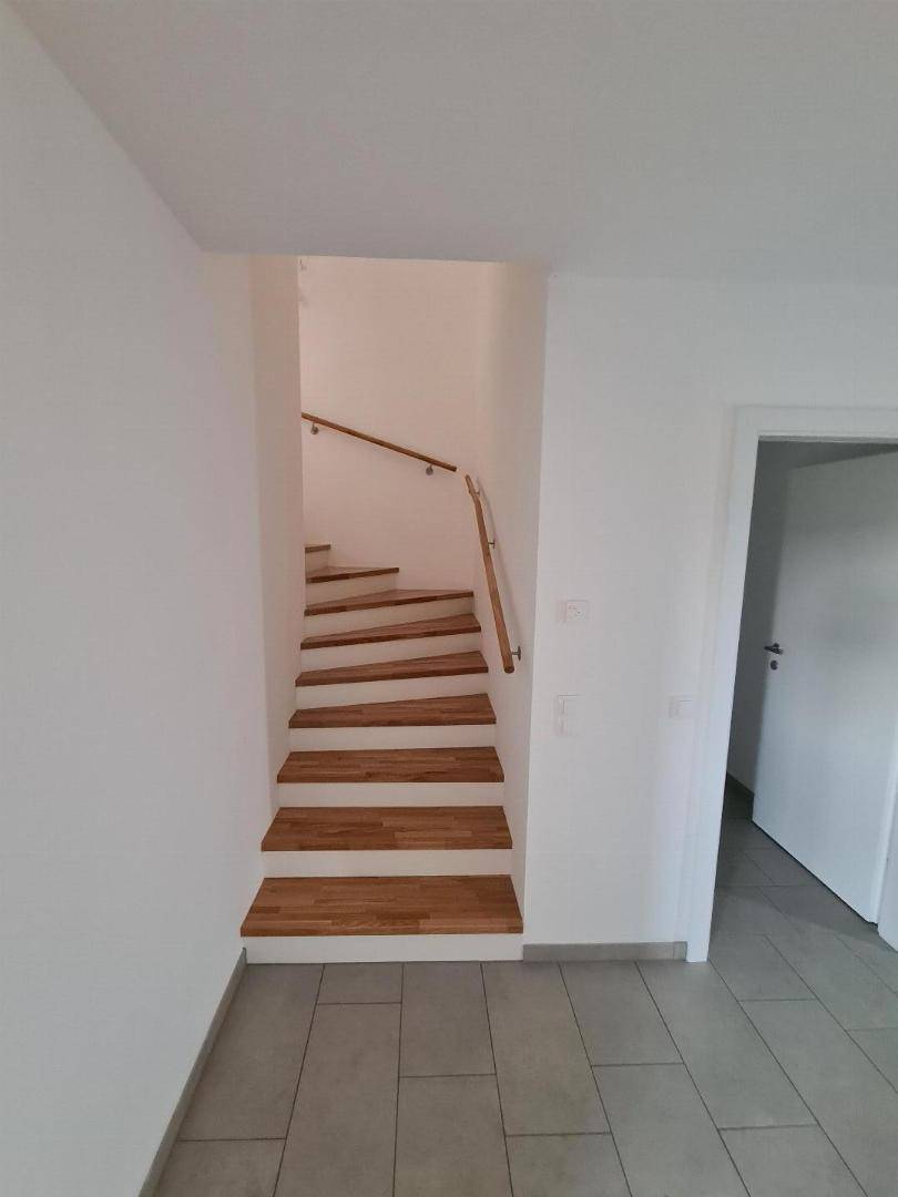 Heller Eingangsbereich mit einer eleganten Holztreppe, die in die obere Etage führt.
