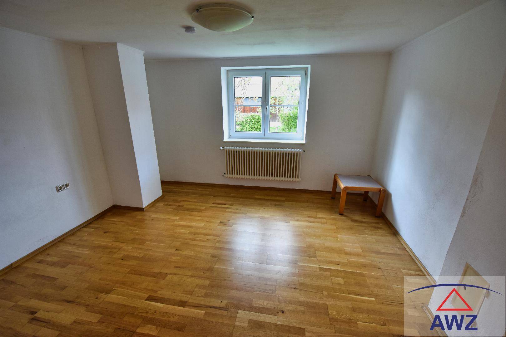 Leeres Schlafzimmer mit Holzboden und einem Fenster, das viel Tageslicht hereinlässt.