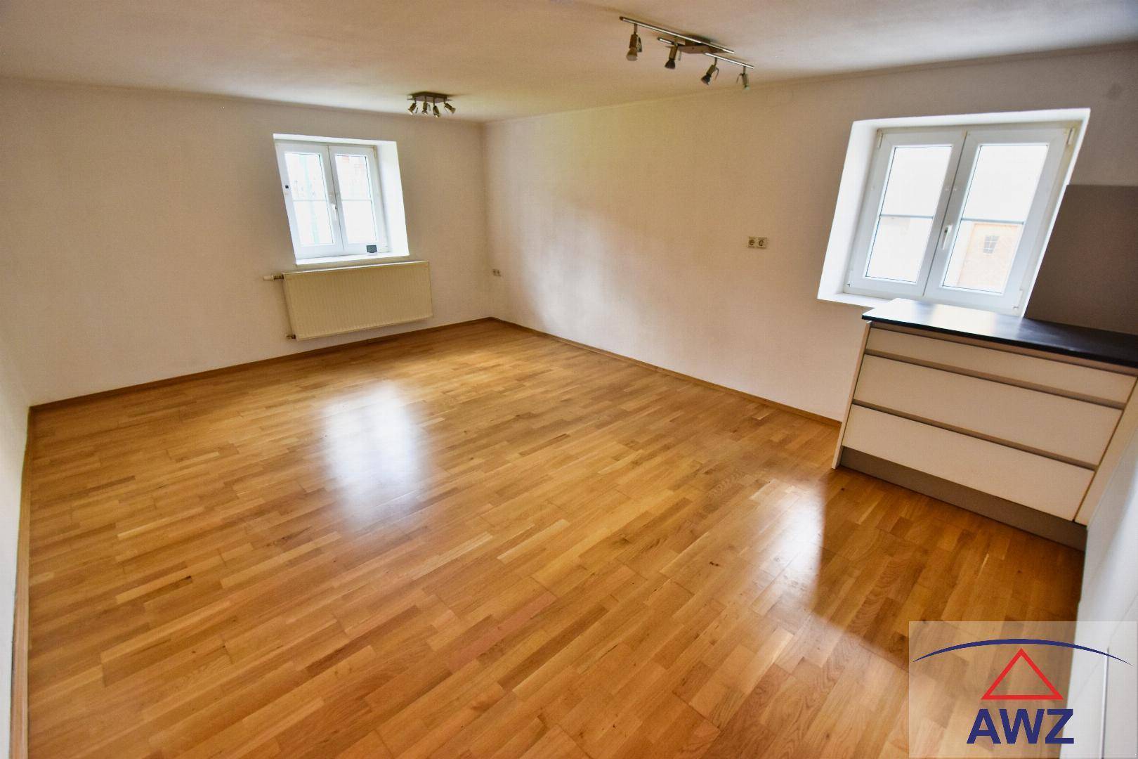 Heller, leerer Raum mit Holzboden und zwei Fenstern, bereit zur individuellen Gestaltung.
