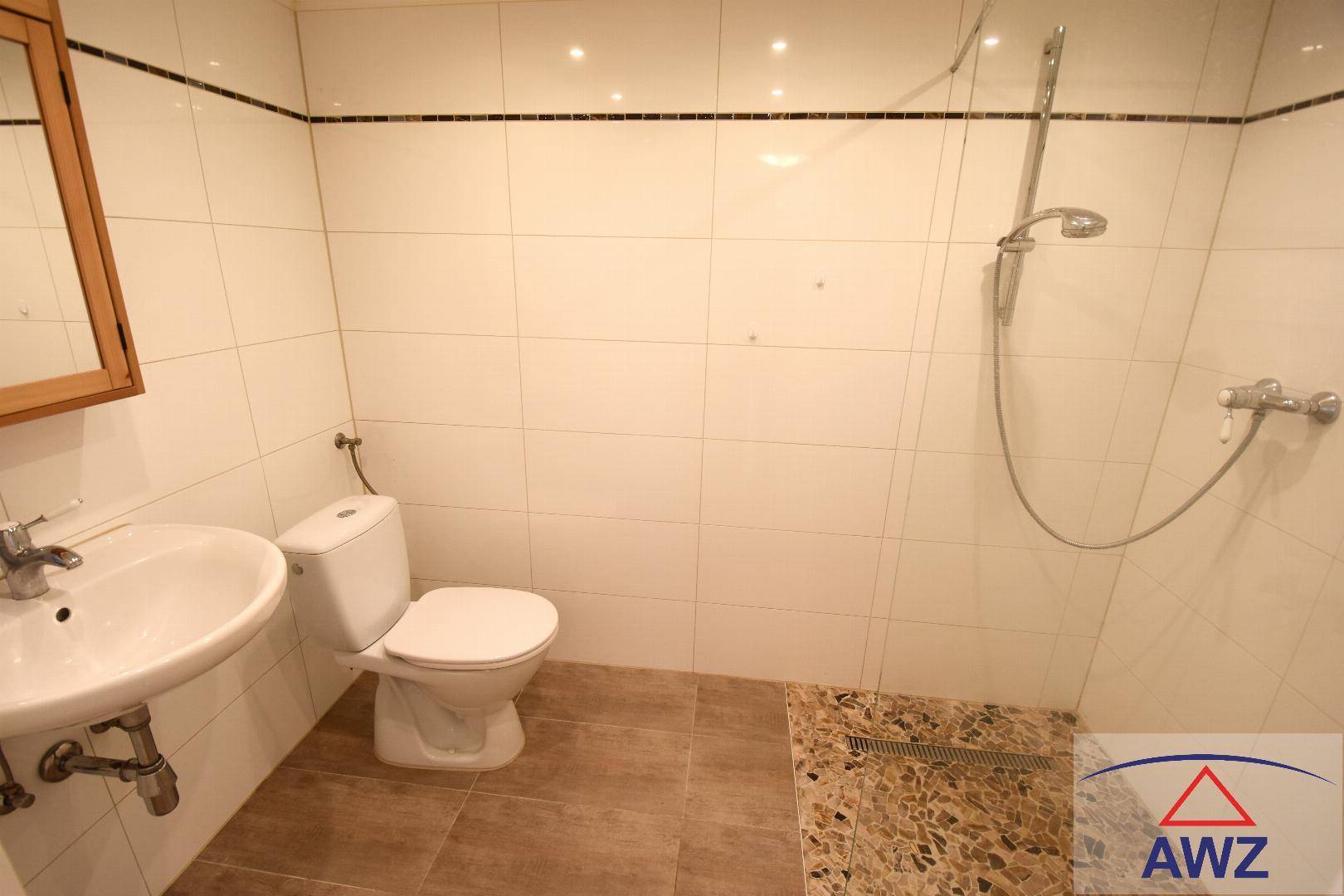 Modern gefliestes Badezimmer mit Dusche, Toilette und Waschbecken in sauberem Zustand.