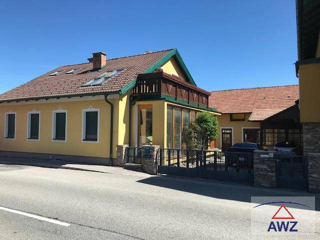 Gelbes Wohnhaus mit rotem Ziegeldach, Wintergarten und kleinem Balkon zur Straße hin.