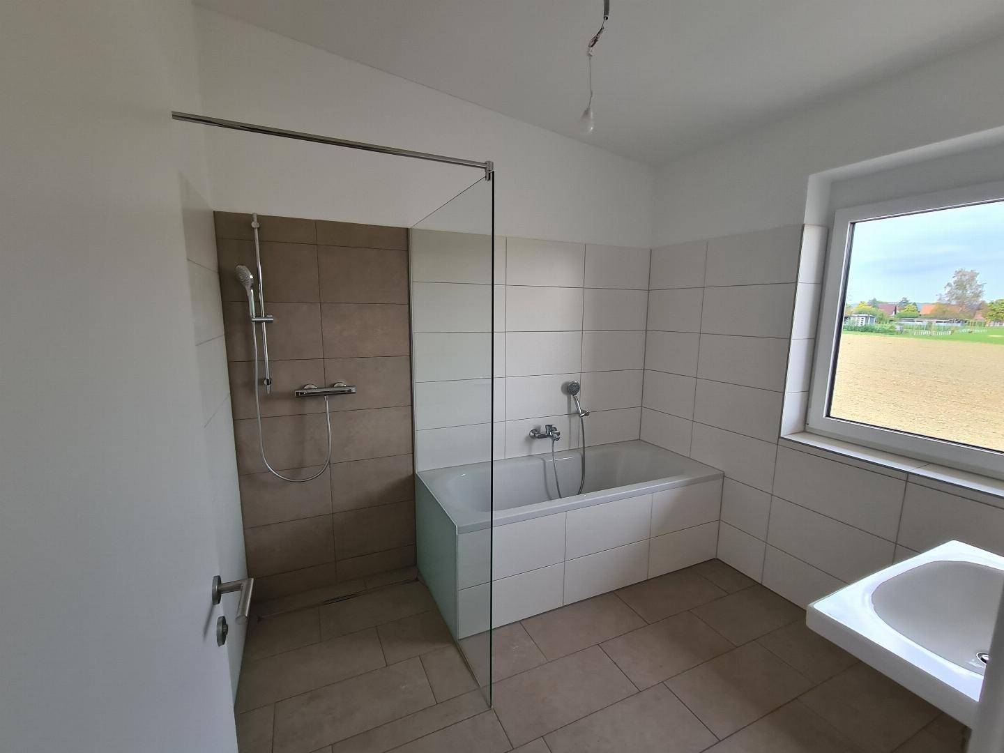 Modernes Badezimmer mit Badewanne, Dusche und Fenster für Tageslicht und Belüftung.