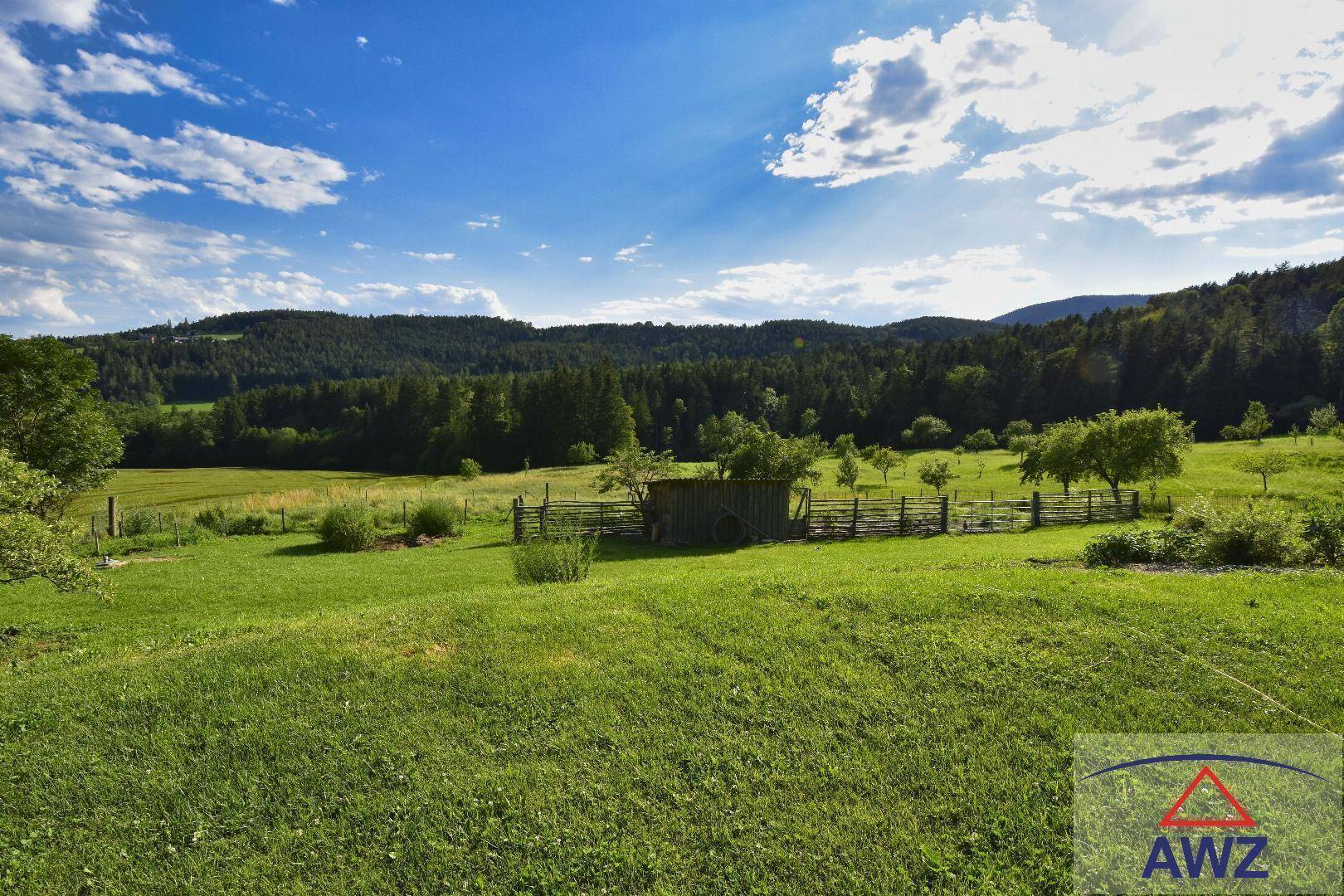 Idyllische Landschaft mit sanften grünen Hügeln, Wäldern und weiten Feldern unter strahlend blauem Himmel.