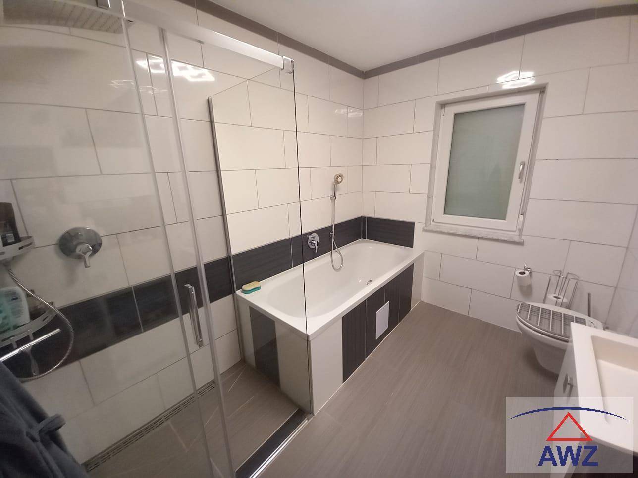 Modernes Badezimmer mit Badewanne, Duschkabine, WC und Fenster in hellen Fliesen.