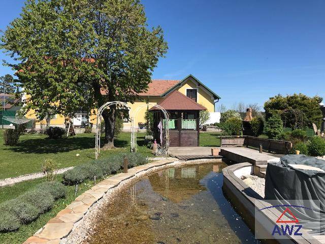 Großer Garten mit Teich, Pavillon und altem Baum vor einem gelben Wohnhaus.