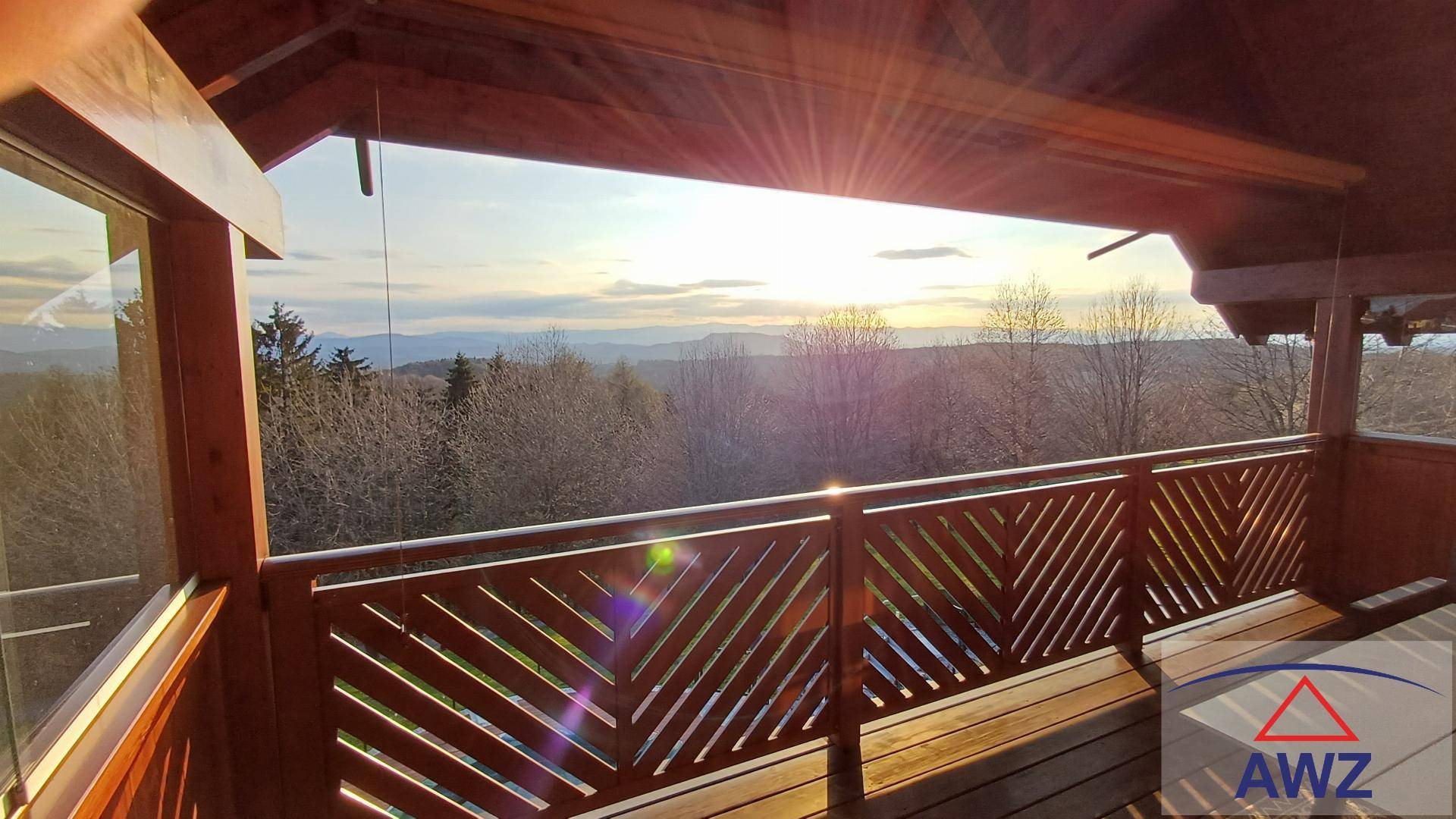 Großer Holzbalkon mit weitem Blick über die Landschaft und Berge bei Sonnenuntergang.