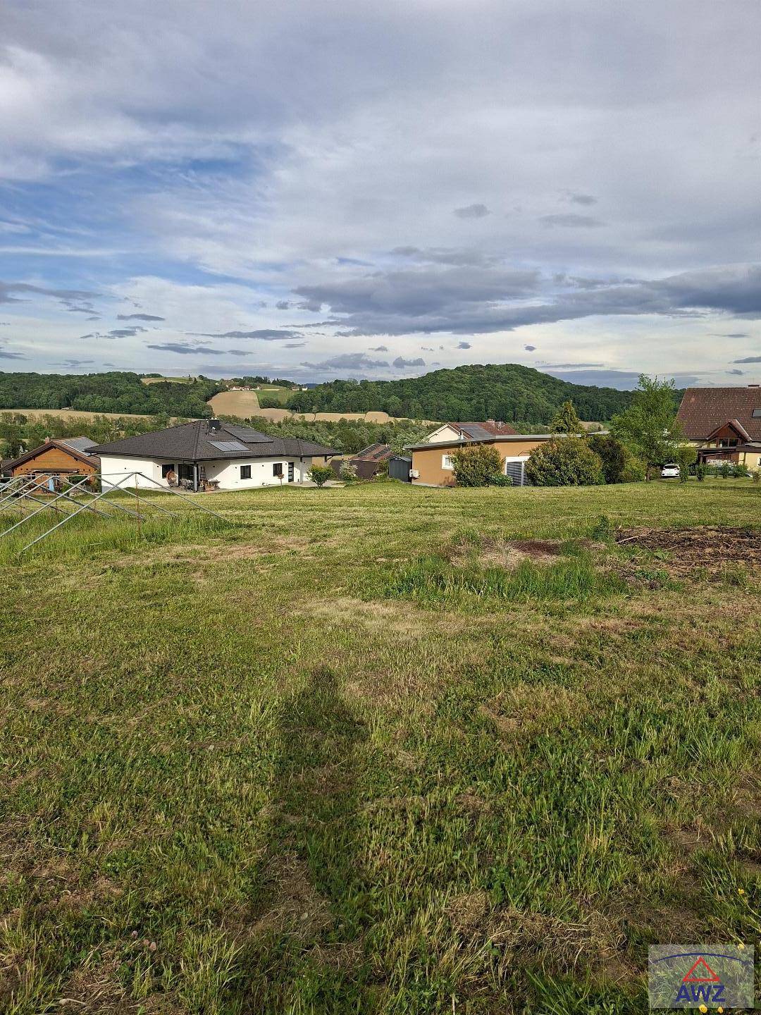 Grünfläche mit Blick auf Wohnhäuser und sanfte Hügel in der Ferne unter einem bewölkten Himmel.