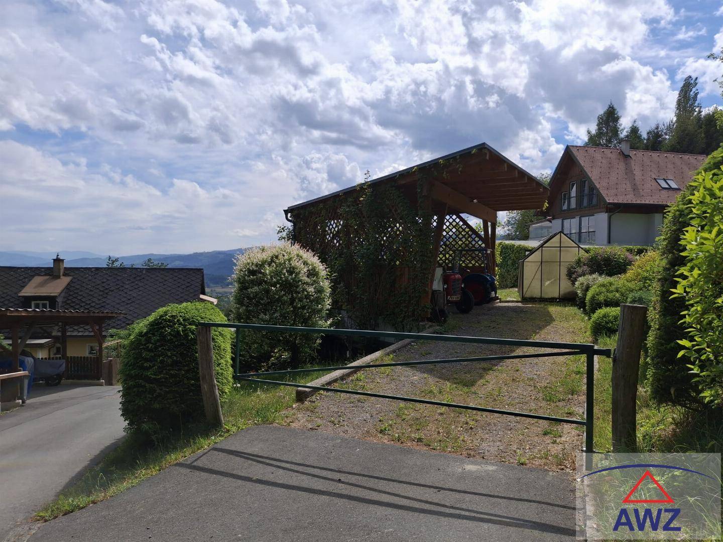 Zufahrt zum Grundstück mit Carport und Gewächshaus, umgeben von grüner Natur und Fernblick.