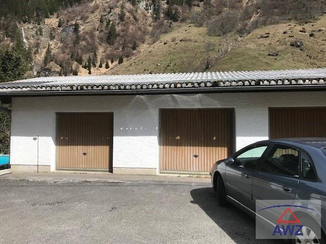 Separate Garage mit drei Holztoren und einem Auto davor, umgeben von alpiner Landschaft.