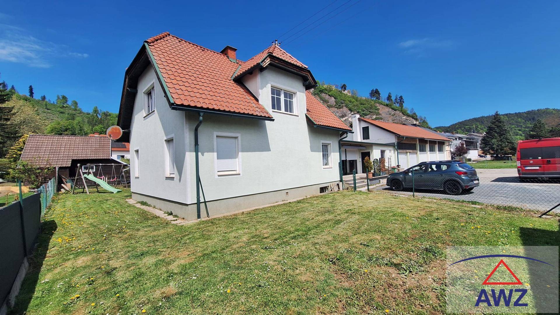 Ansicht des Hauses von vorne mit geparktem Auto und einem grünen Hügel im Hintergrund.