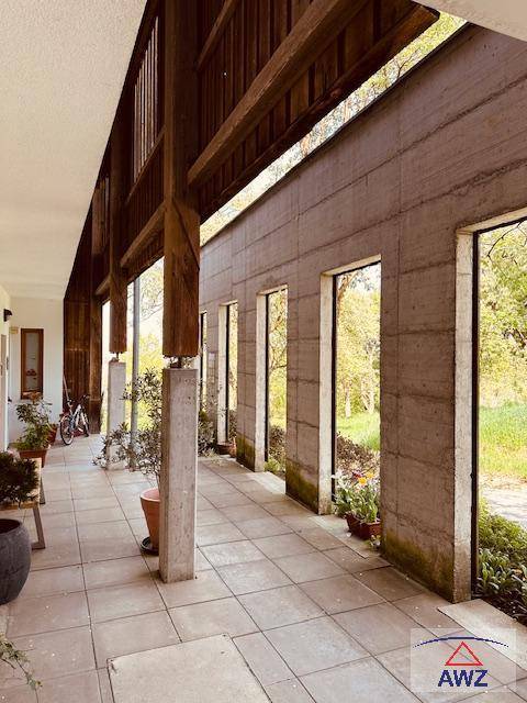 Überdachte Loggia mit Fliesenboden und Blick ins Grüne, gesäumt von Topfpflanzen und natürlichem Licht.