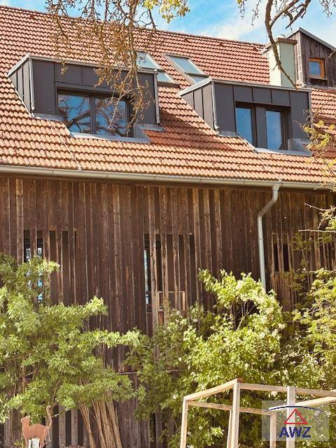 Detailansicht der Holzfassade eines Hauses mit traditionellem Ziegeldach und modernen Dachgauben.