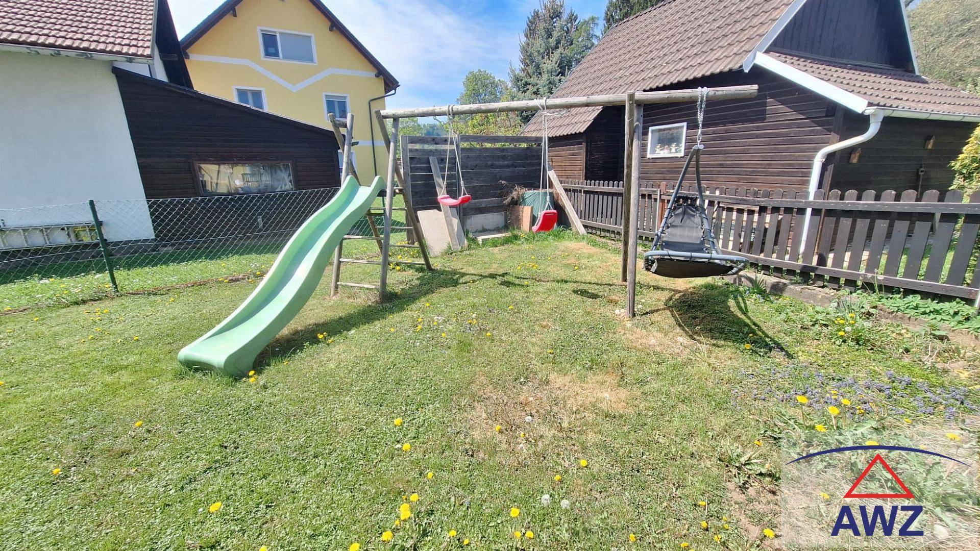 Kinderspielplatz im Garten mit Rutsche und Schaukeln, umgeben von einer grünen Rasenfläche.