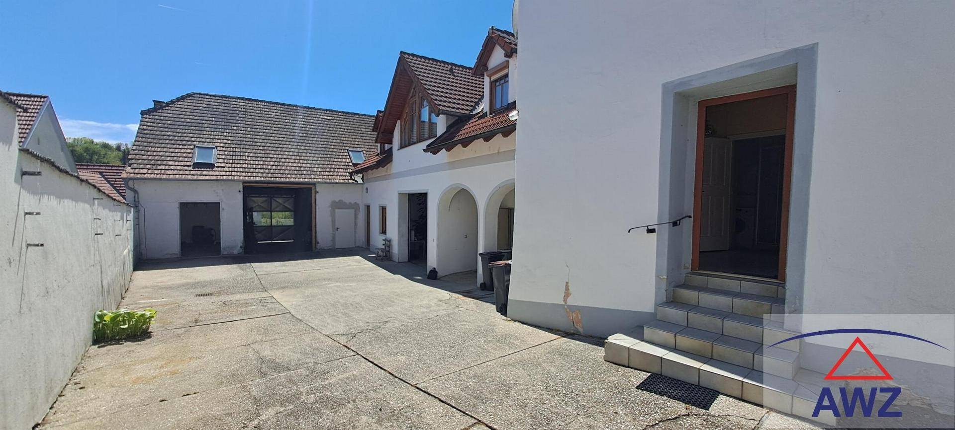 Anwesen mit mehreren Gebäuden, gepflastertem Innenhof und Eingangsbereich mit Treppe.