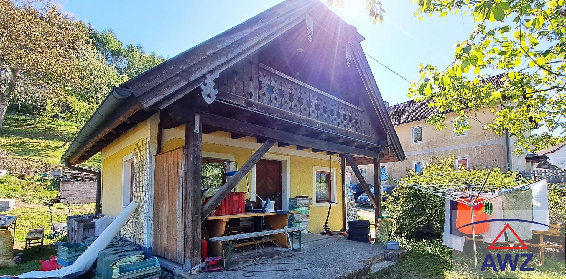Kleines Nebengebäude mit traditionellem Holzbalkon und Wäscheleine im sonnigen Gartenbereich.