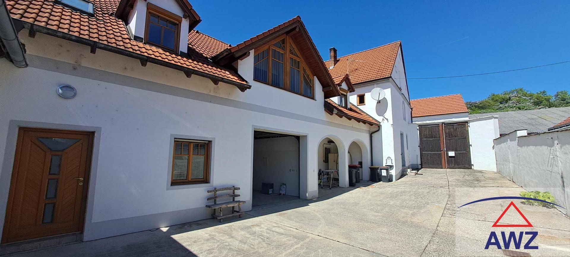 Weißes Gebäude mit roten Ziegeldächern, Holztüren und gepflastertem Hofbereich.