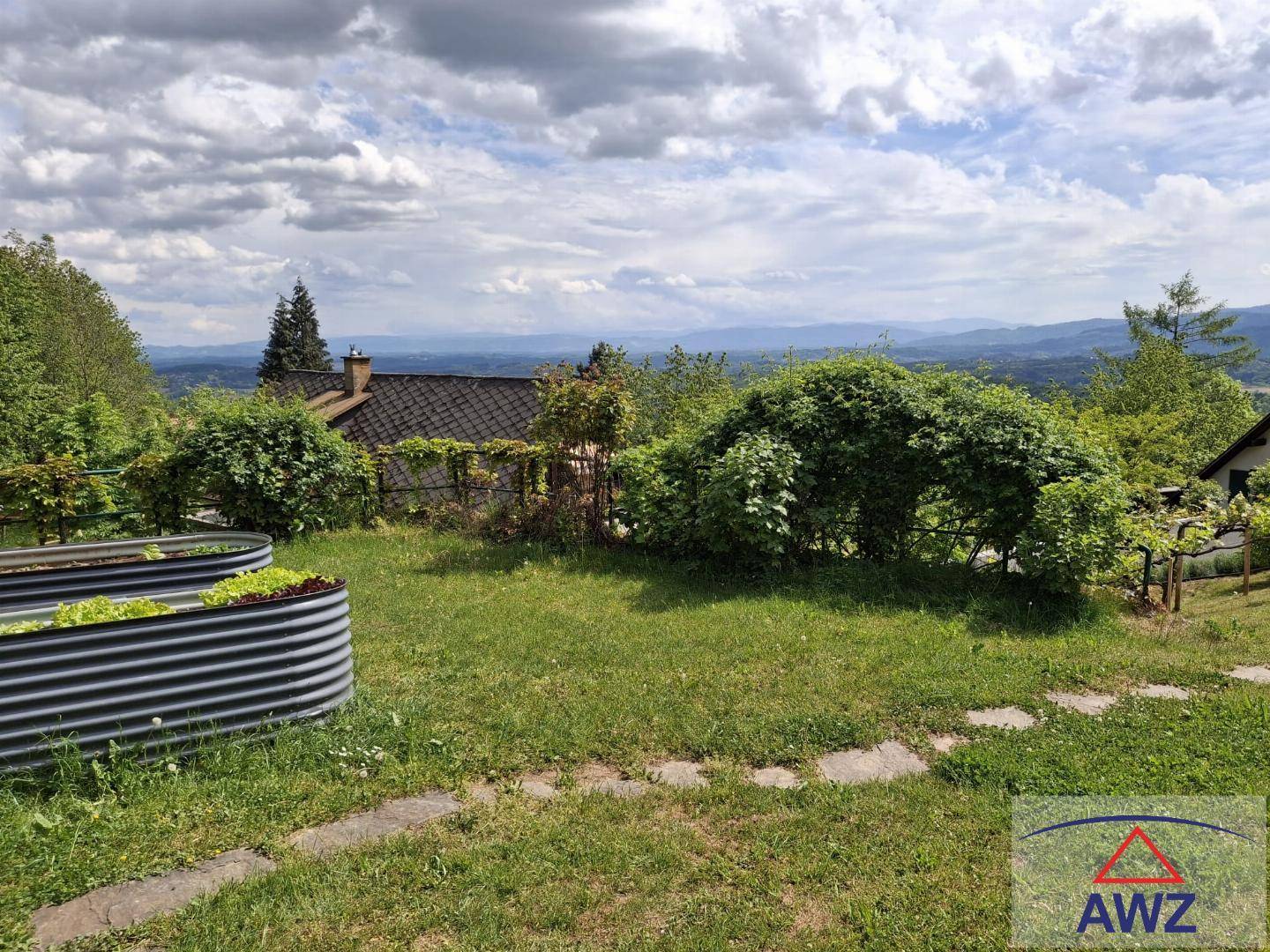 Gartenbereich mit Hochbeet und Rasenfläche, umgeben von üppigem Grün und einem weiten Blick in die Ferne.