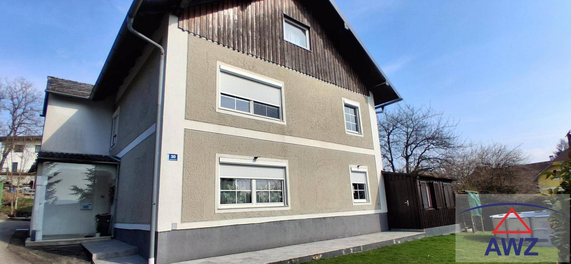 Seitenansicht des Einfamilienhauses mit Rollläden und gepflegter Fassade unter blauem Himmel.
