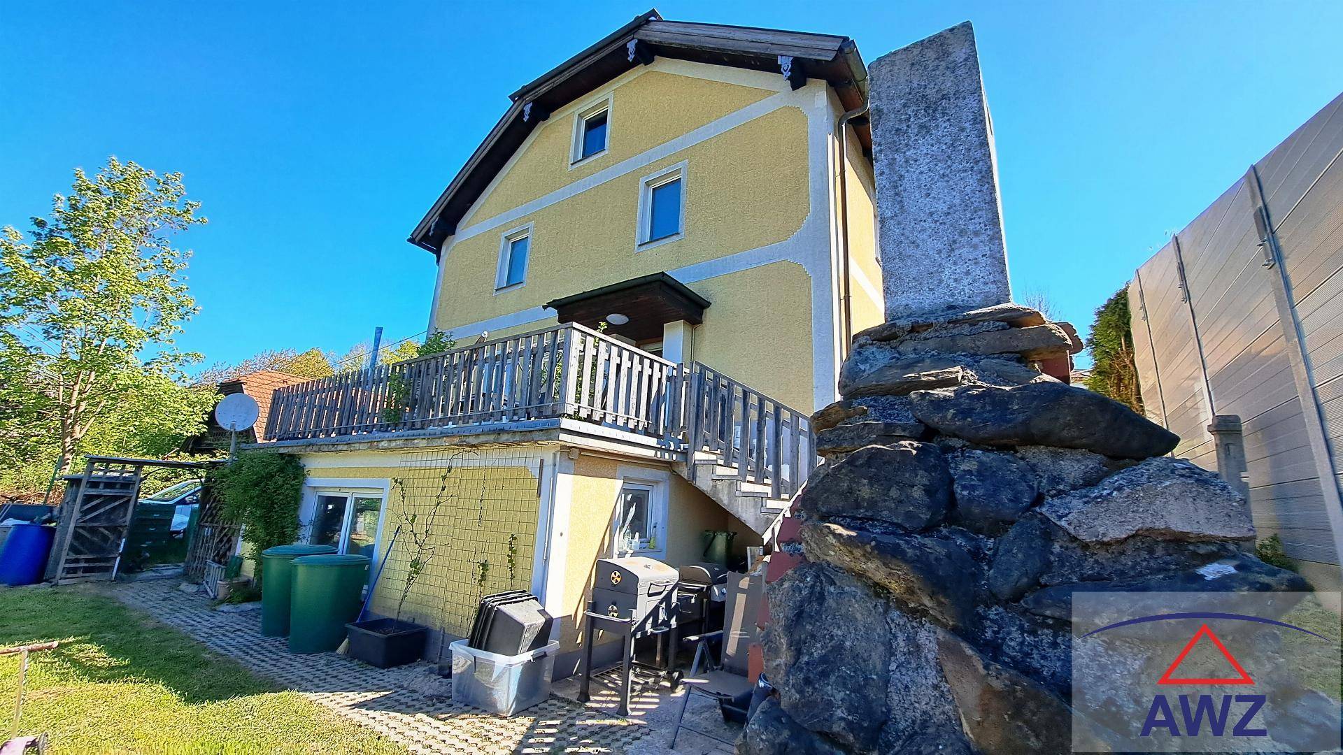 Rückseite des Hauses mit Außentreppe, Balkon und einem kleinen Terrassenbereich mit Grill.