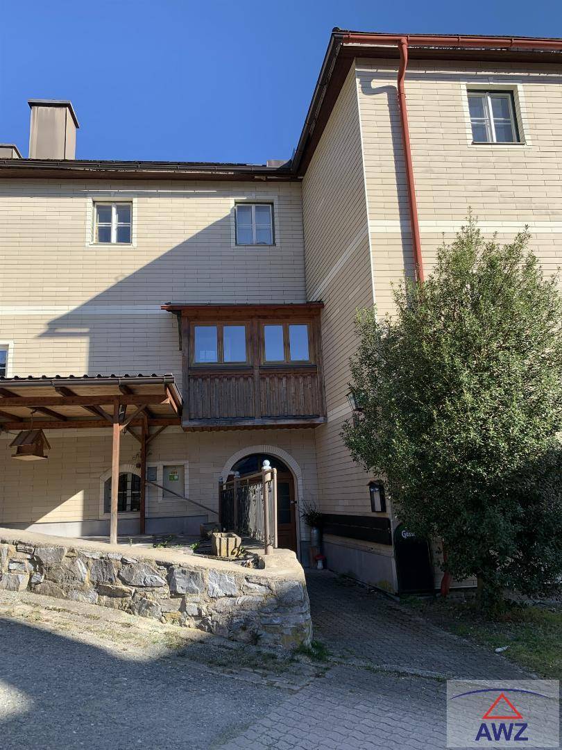 Seitenansicht des Gebäudes mit heller Fassade, Holzverkleidung und einem kleinen Holzbalkon.