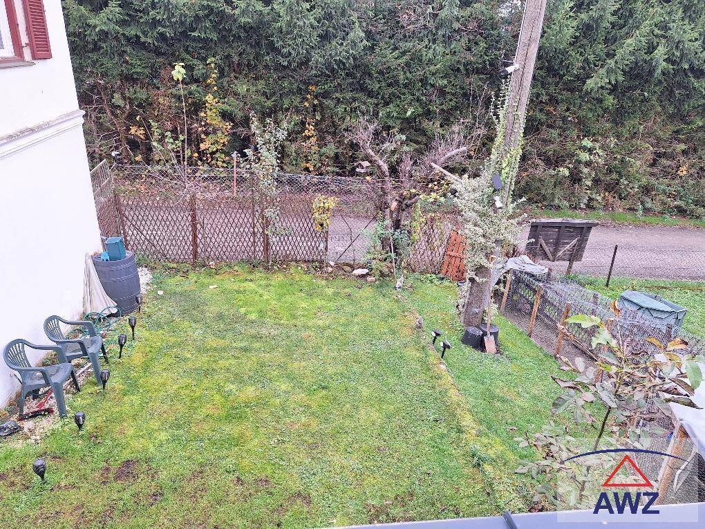Kleiner Gartenbereich mit Rasenfläche, Zaun und einigen Gartenstühlen.