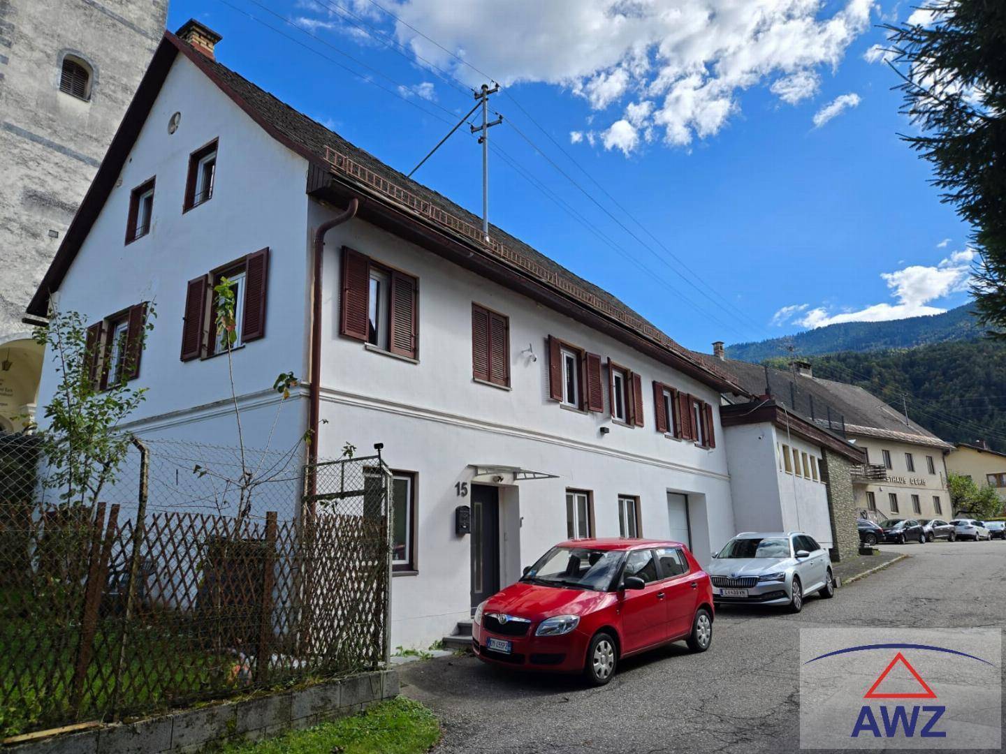 Traditionelles weißes Wohnhaus mit braunen Fensterläden und Bergblick im Hintergrund.