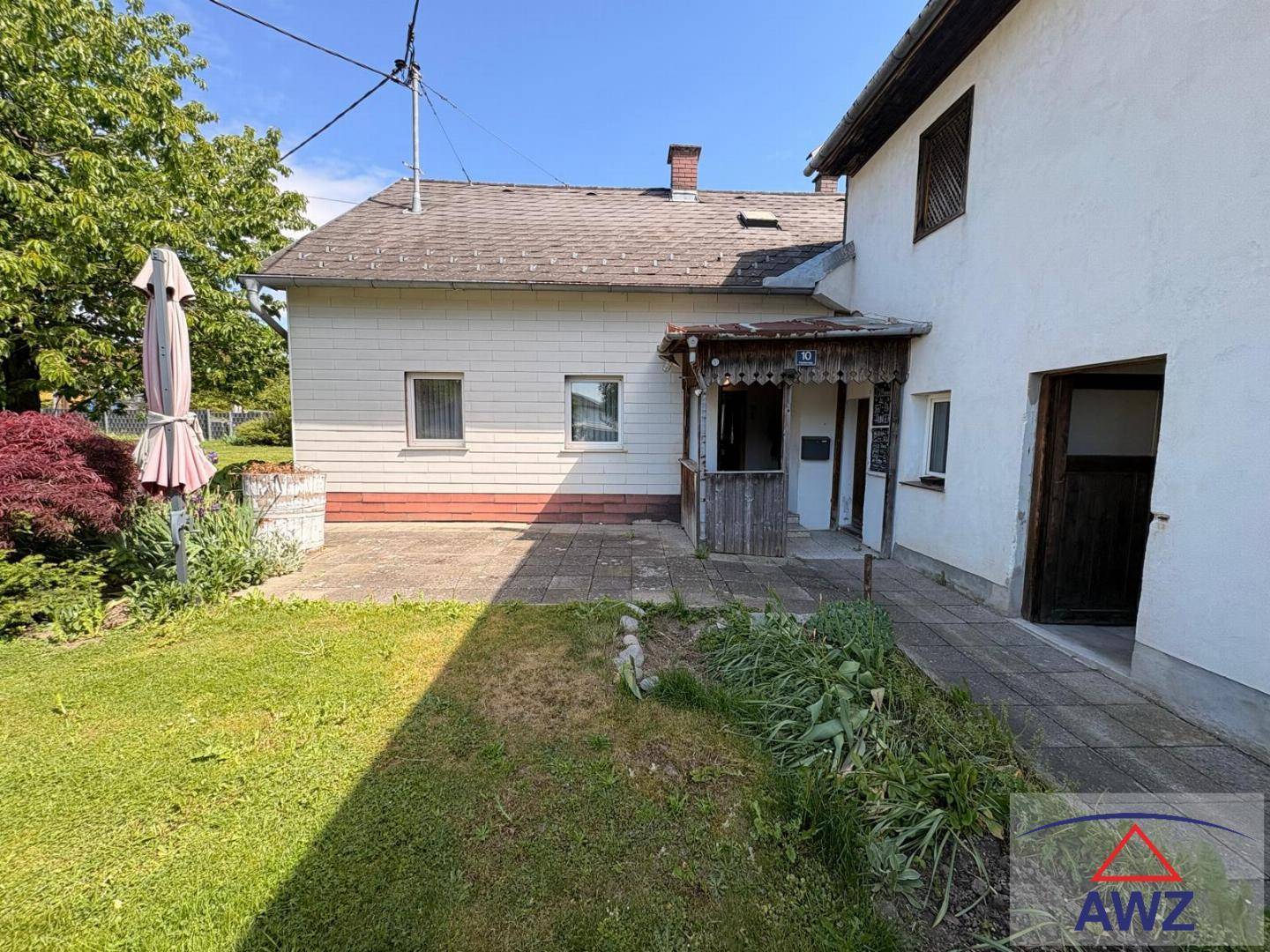Seitenansicht eines Hauses mit grünem Rasen, Gartenbereich und einem kleinen Vordach am Eingang.