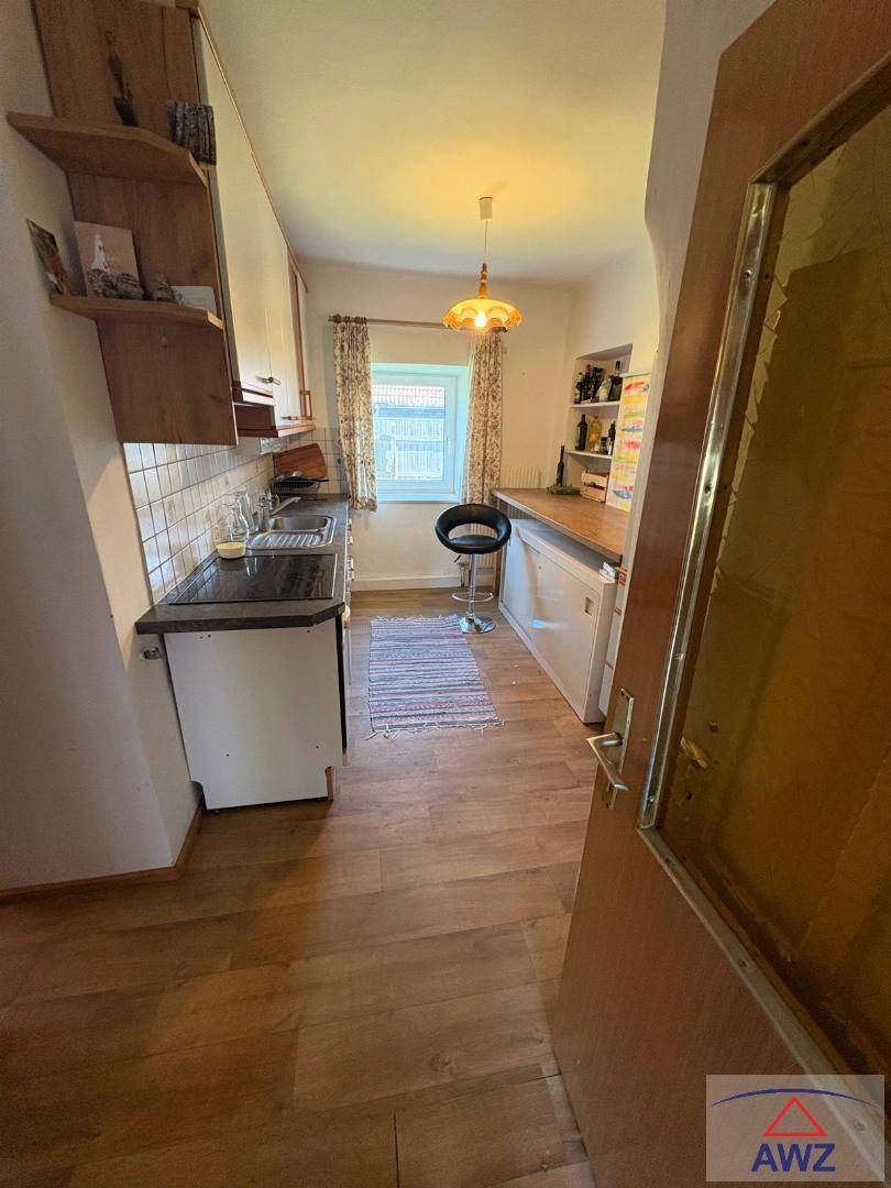 Kleine, funktionale Küche mit Holzboden, Einbauschränken und einem Fenster mit Vorhängen.