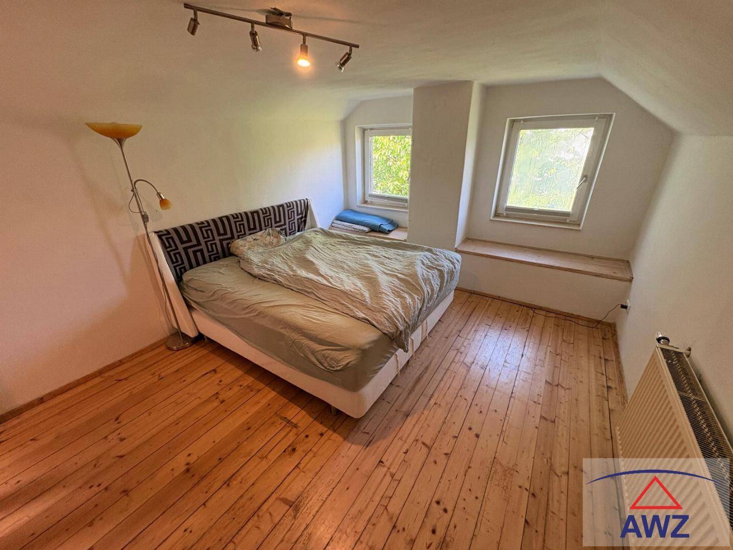 Gemütliches Schlafzimmer im Dachgeschoss mit Holzdielenboden, schrägen Wänden und zwei Fenstern.