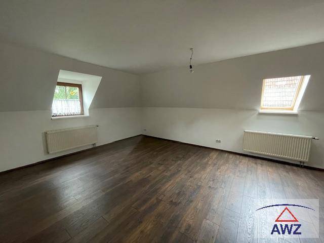 Helles Zimmer im Dachgeschoss mit dunklem Laminatboden und zwei Dachfenstern.