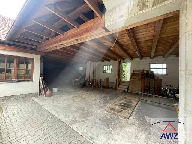 Großer offener Raum mit Holzbalken, Betonboden und Fenstern, möglicherweise als Garage oder Werkstatt nutzbar.