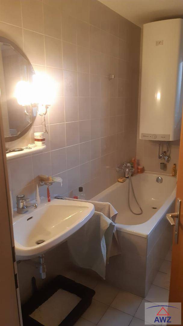 Badezimmer mit Badewanne, Waschbecken und hellgrauen Wandfliesen, ausgestattet mit einem Boiler.