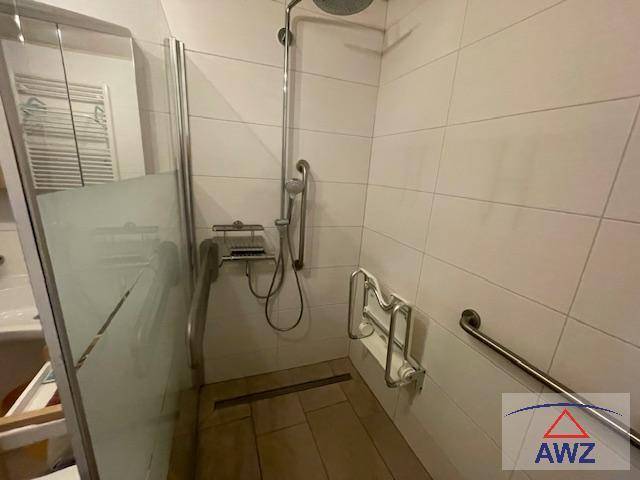 Modernes Badezimmer mit ebenerdiger Dusche, weißen Fliesen und Haltegriffen für Barrierefreiheit.