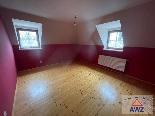 Leeres Zimmer mit roten Wänden, Holzdielenboden und zwei Fenstern unter Dachschrägen.